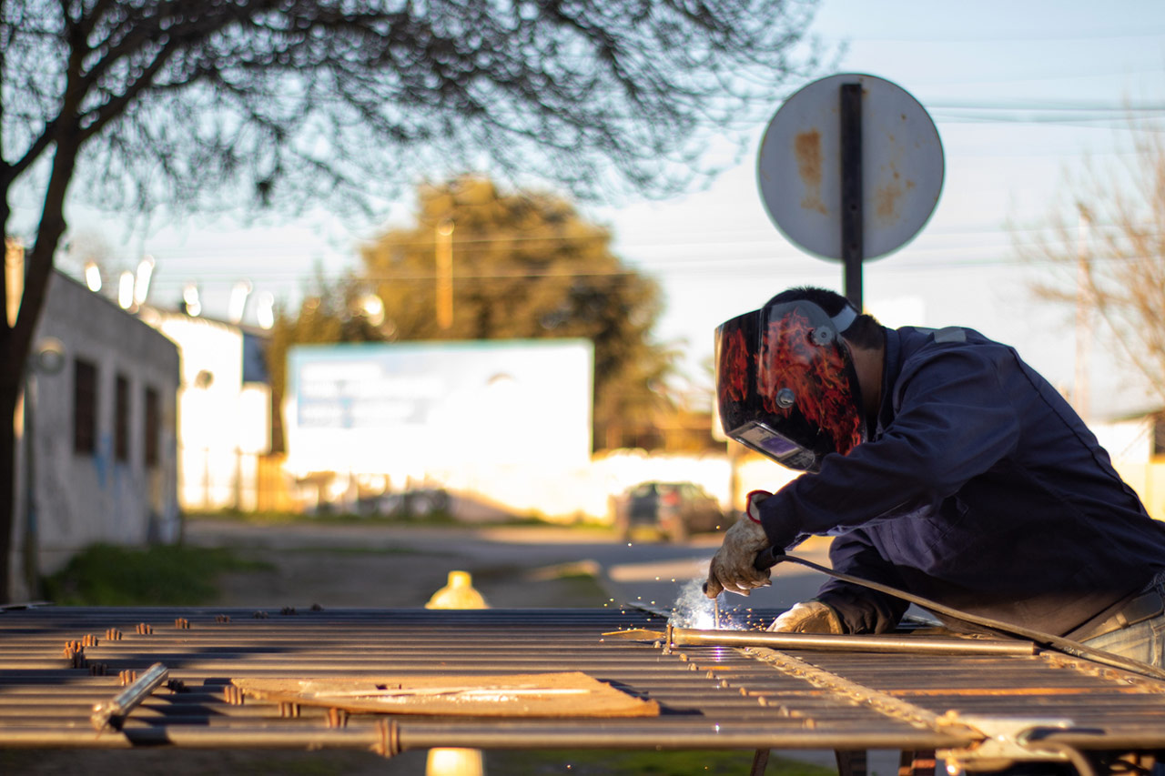 a welder wearing a welding mask and protective glove repairing a steel fence, welding broken braces